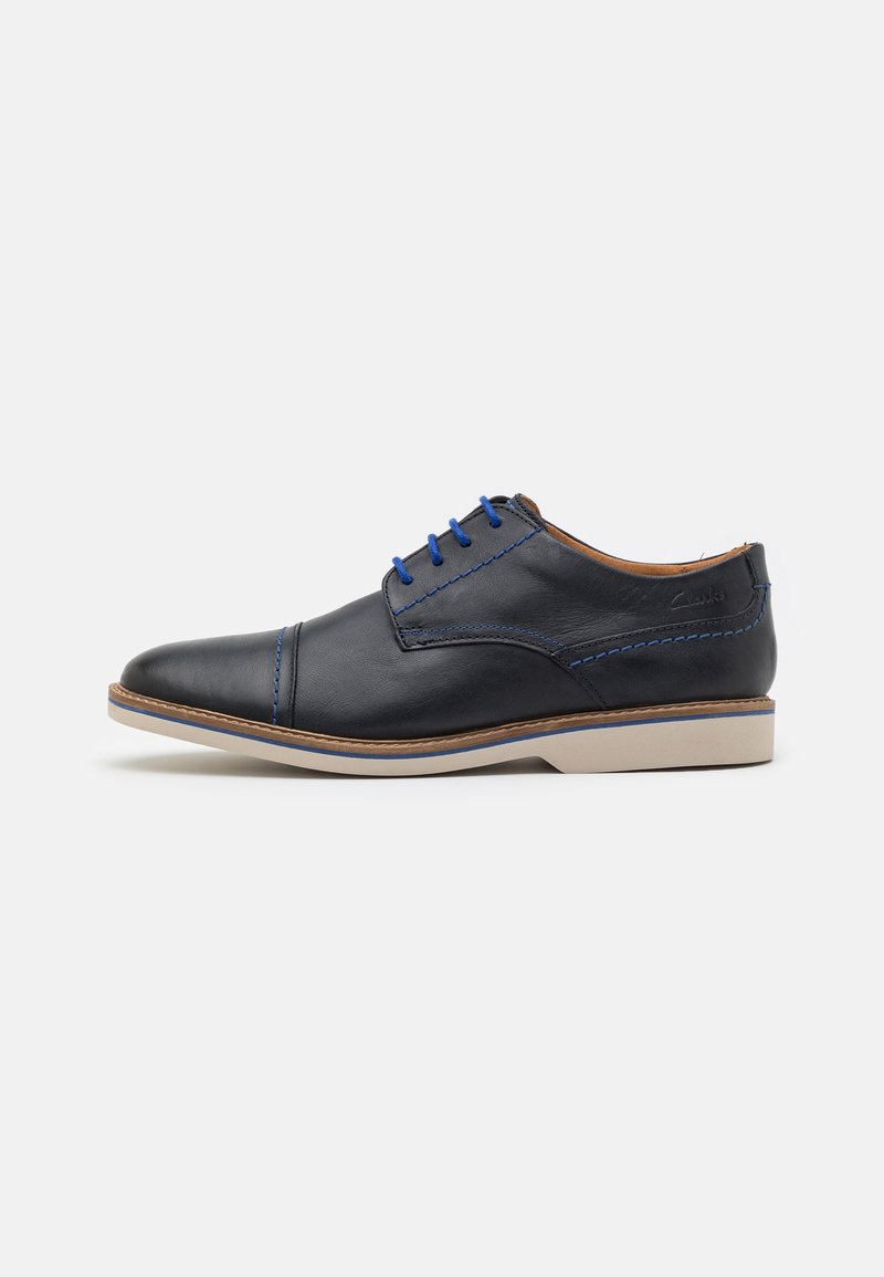 Chaussure habillée noire en cuir à lacets avec surpiqûres et lacets bleus, intérieur beige, semelle beige avec un petit talon, vue de côté.