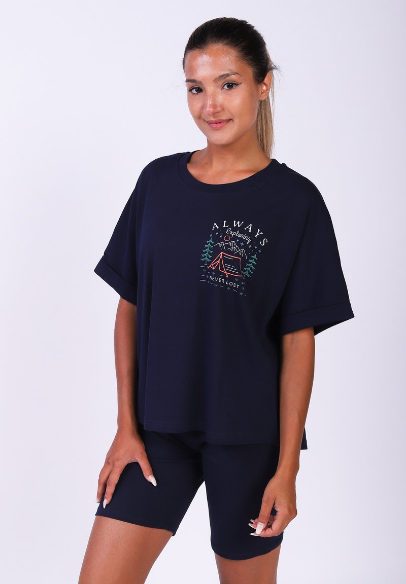 T-shirt en coton bleu marine avec des manches courtes retroussées et un imprimé graphique mettant en avant des arbres et une tente ; associé à un short de vélo bleu marine ajusté.