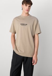 Beez värvi puuvillane T-särk ümarate kaelustega, lühikeste varrukatega ja musta "BARBOUR INTERNATIONAL" logoga rinnal.