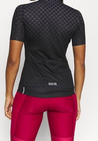 Jersey de ciclismo negro de manga corta con patrón geométrico, que presenta un diseño ajustado y costuras planas. Logo en la parte posterior, combinado con mallas burdeos.