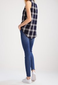 Top sin mangas de cuadros en azul marino y blanco, combinado con jeans ajustados azules y zapatillas blancas. Tejido texturizado con detalle de dobladillo asimétrico.