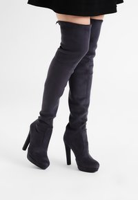 Stivali in suede viola scuro fino al ginocchio con punta a mandorla e alto tacco a stiletto; texture liscia e cuciture decorative minime.