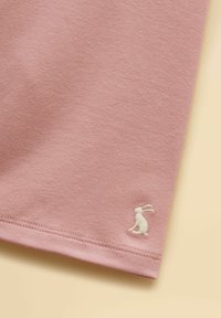 Coin d'un tissu rose avec ourlet cousu et petit lapin blanc brodé près du bord sur un fond beige clair.