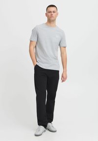T-shirt gris à col rond avec des manches courtes, associé à un pantalon noir et des baskets blanches. Le tissu semble doux et confortable, avec peu de marquage visible.