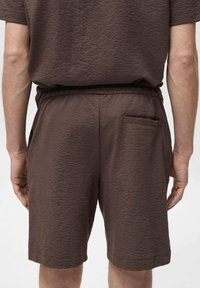 Shorts marron à texture avec une taille élastique et une poche arrière unique, coutures visibles et une coupe décontractée.