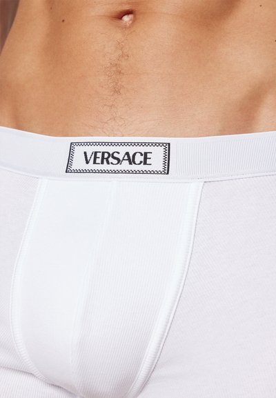 Boxeri scurți albi din bumbac, cu o textură ribbată și un logo Versace negru pe o talie albă.