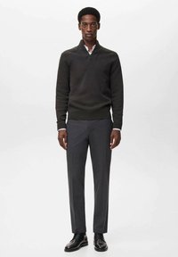 Mørkegrøn strikket sweater med høj halsudskæring, parret med grå skrædderbukser og sorte snørebåndssko. Simple, rene designelementer.