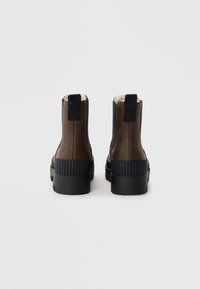 Bottines en cuir marron avec des panneaux latéraux élastiques noirs, des semelles en caoutchouc texturé et des languettes à l'arrière pour un enfilage facile.