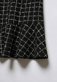 Tela negra texturizada con un patrón de cuadrícula blanca, ligeramente doblada, proyectando sombras sobre una superficie clara.