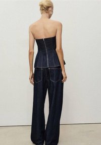 Top de corsé de mezclilla con una silueta ajustada y dobladillo de peplum, combinado con pantalones de mezclilla oscuros de cintura alta, holgados y con bolsillos traseros.