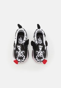 Černobílé nazouvací boty s designem psí tváře, obsahující měkké uši, pohyblivé oči a akcent v podobě červeného jazyka. Gumová podrážka.