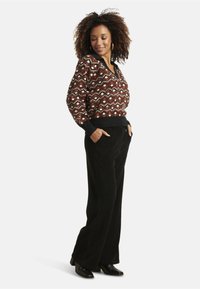 Brown patterned pullover with geometric shapes, knit texture, and black cuffs; paired with black corduroy wide-leg pants and ankle boots.