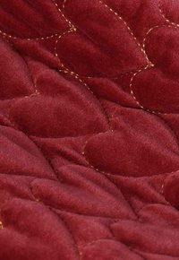 Roter Stoff mit weicher Textur, der ein gestepptes Design aus überlappenden Herzformen aufweist, akzentuiert mit goldenen Stichen.