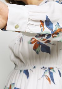 Vestido blanco con estampados en azul, naranja y verde, con puños abotonados y cintura fruncida para un ajuste relajado.