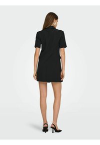Crna haljina s kratkim rukavima, prilagođenog kroja, koja ima ovratnik i strukirana je, uparena s crnim sandalama na visoku petu.