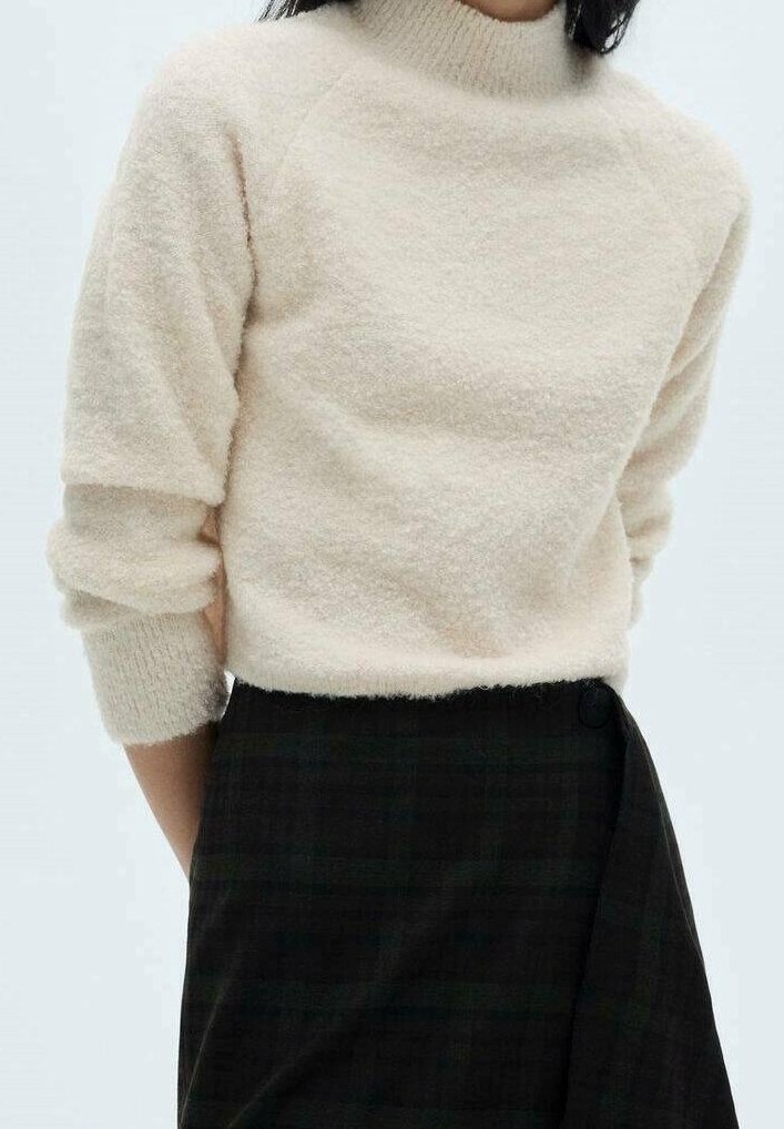 Kermansatteinen, pehmeä neule, jossa on korkea kaulus ja kolmivartiset hihat. Yhdistetty tummatarkoitukselliseen ruudulliseen hameeseen, jossa on sivunapit.