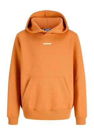 Garçon debout portant un sweat à capuche orange, un pantalon noir à jambes larges et des baskets blanches sur un fond clair uni.