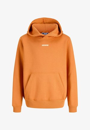 Dreng står iført en orange hættetrøje, sorte bukser med vidde og hvide sneakers på en ensfarvet lys baggrund.