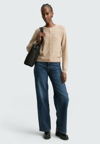 Cárdigan de punto beige con cuello redondo, cierre de botones y mangas largas, combinado con jeans de mezclilla azul de pierna ancha y un bolso negro de hombro.