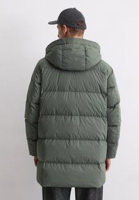 Vooderdatud roheline parka, millel on kapuuts ja millel on tikand. Kangas on sile ja ääred ulatuvad puusast allapoole.