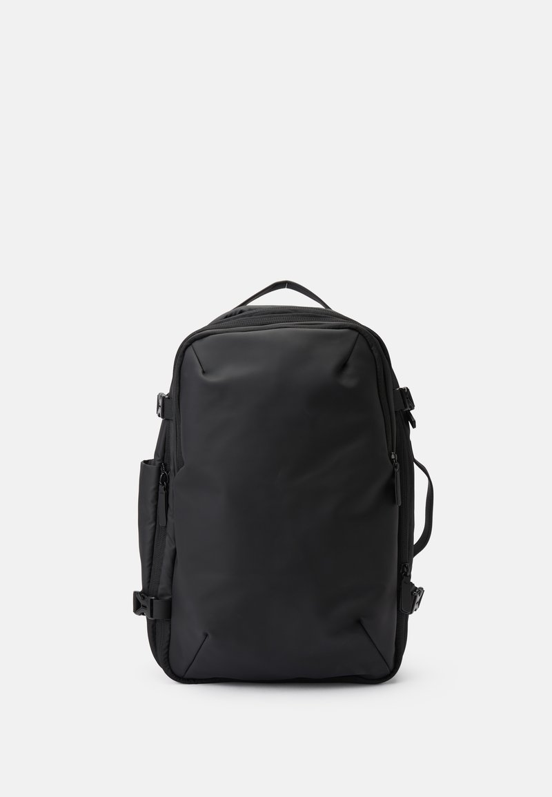 Mochila negra hecha de tela resistente al agua, con forma rectangular, múltiples compartimentos con cremallera y un asa de transporte en la parte superior.