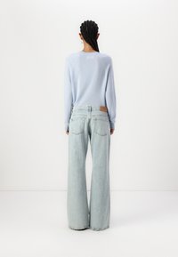 Light blue knitted sweater with long sleeves, paired with light wash, wide-leg denim jeans featuring back pockets and a leather patch.