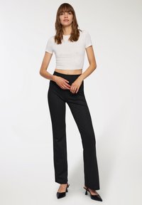 Biała krótka bluzka z krótkim rękawem ozdobiona małymi ćwiekami, w połączeniu z dopasowanymi czarnymi spodniami w prążki i czarnymi szpilkami, charakteryzującymi się klasycznym prostym krojem.