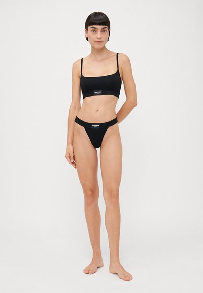 Black bra and thong set made of smooth fabric; bra has thin straps and a logo band; thong features a similar band design.