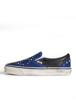 Sneaker slip-on blu e nero con suola bianca, decorata con piccoli borchiette bianche e argento, leggermente consumata sulla suola.