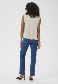 Top beige sans manches avec une coupe décontractée, associé à un jean en denim bleu. Le jean présente une coupe droite et un design de poche classique.