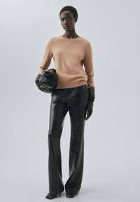 Lichtroze wollen trui gecombineerd met zwarte, high-waisted leren broek. Model accessoriseert met een zwarte pouch en leren handschoenen.