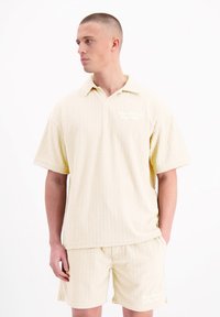 Kortebloesem, met kraag, en bijpassende short in lichtgeel met een subtiele textuurpatroon en een logo-accent op de borstzak.