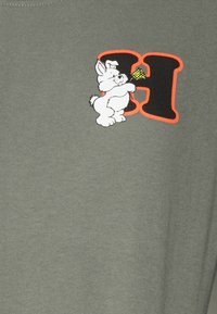 Olivgrünes T-Shirt mit einem weißen Cartoon-Kaninchen, das ein Eis cone hält, neben einem fetten, schwarzen Buchstaben "H", umrandet in Orange.