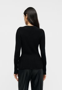 Μαύρο πλεκτό πουλόβερ με μακριά μανίκια, ριμπ λαιμόκοψη και τελείωμα με βολάν. Λείος υφής, εφαρμοστό σχέδιο και μινιμαλιστικό στυλ.