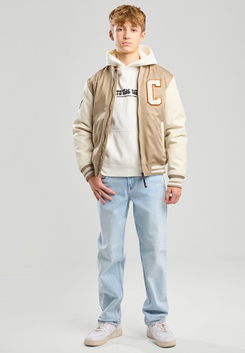 Beige varsity-takki vaaleilla hihansuilla, rinta  iso "C", valkoinen huppari tekstillä, vaaleansiniset farkut ja valkoiset lenkkarit.