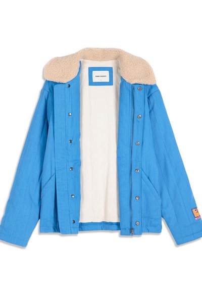 Veste bleue avec col en polaire beige, boutons-pression, fermeture éclair, doublure intérieure blanche visible et un petit patch sur la manche gauche.