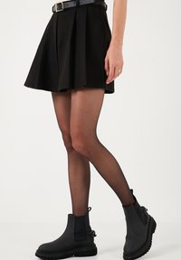 Čierna mini sukňa s rozšíreným spodným okrajom a skladmi, v kombinácii s nepriehľadnými čiernymi pančuchami a masívnymi čiernymi členkovými topánkami s bočnými elastickými panelmi a ťahacími pútkami.