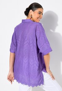 Tunic viola con maniche corte, caratterizzata da motivi esagonali ricamati e orlo a scallop. Tessuto leggero con una texture liscia.