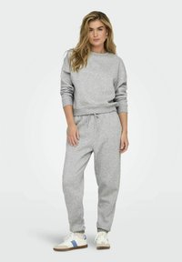 Grijze katoenen sweatshirt en bijpassende joggingsbroek met een trekkoord in de taille; heeft ribgebreide boorden en een relaxte pasvorm. Gecombineerd met sneakers.