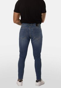 Vaqueros ajustados de mezclilla azul con cintura de altura media, diseño de cinco bolsillos y tejido texturizado. Cuenta con bolsillos traseros cosidos y etiqueta negra en la cintura.