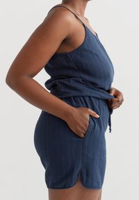 Navyblauer Jumpsuit aus strukturiertem Stoff, mit dünnen Trägern, tailliertem Schnitt und seitlichen Taschen, lockerer Passform und seitlichen Schlitzen.