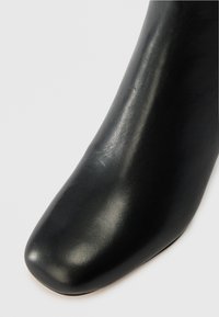 Juodas odinis kulkšninis botas su smailiu nose, lygia tekstūra ir elegantišku dizainu, su žemu kvadratiniu kulnu, užtikrinančiu stabilumą.