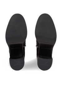 Zapatos de cuero negro con suelas planas. La parte inferior presenta un acabado suave con un logotipo grabado en los tacones y una textura de agarre con un patrón.