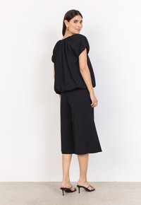 Svart outfit bestående av en löst sittande, kortärmad topp med rundad halsringning och matchande vida byxor, båda i ett mjukt tyg.