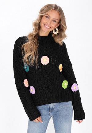 Schwarzer Strickpullover mit hohem Kragen und bunten Blumen-Applikationen in Pink, Teal, Gelb, Lila und Grün. Rippbündchen und Saum.