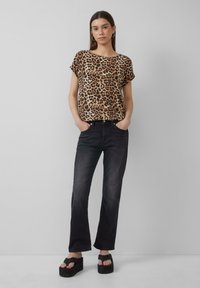 Blouse à manches courtes en imprimé léopard, fabriquée en tissu léger, associée à un jean large en denim foncé et des sandales à plateforme.