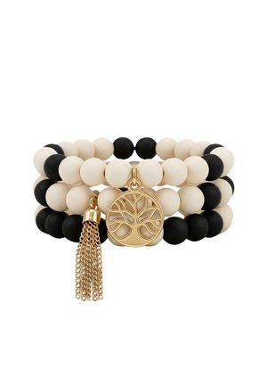 Bracelets empilés de perles noires et blanches avec un charme arbre de vie doré et un pompon en chaîne dorée.