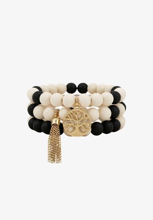 Bracelets empilés de perles noires et blanches avec un charme arbre de vie doré et un pompon en chaîne dorée.