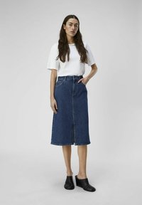 Denim skjørt med en midtlengde design, frontslitt og rå kant; parret med en løs hvit t-skjorte og svarte kilehæler.