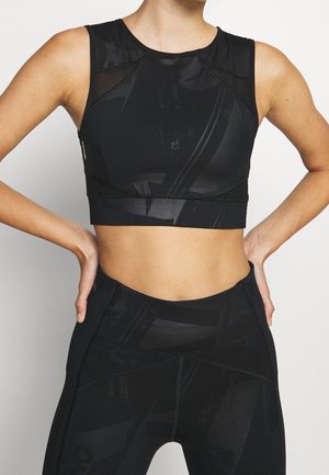 Mujer con un top corto sin mangas de estampado negro y leggings de cintura alta a juego, con las manos apoyadas en las caderas.